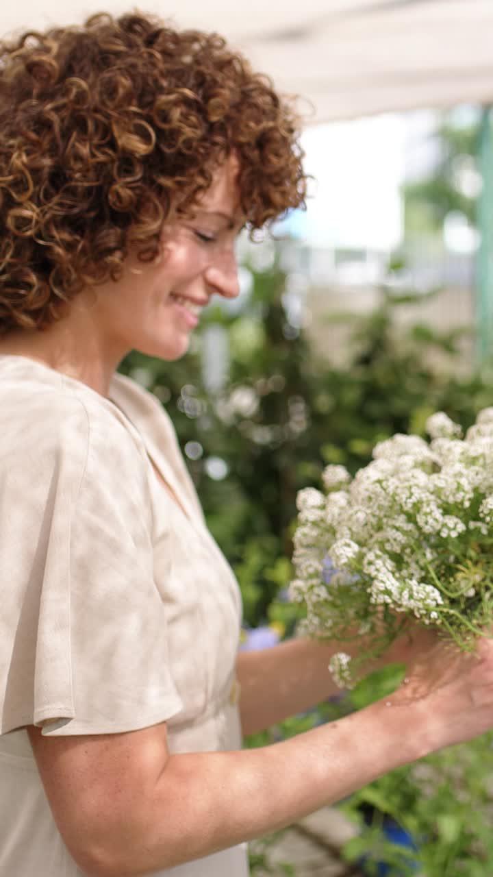 Florist holding and smelling white flowers in greenhouse. Vertical