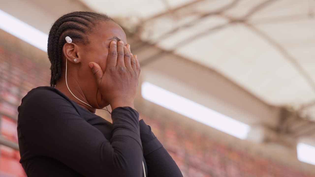 Wanita berkulit hitam di stadion menutupi wajahnya, menggambarkan perannya sebagai penonton, pelajar, pendukung, atau orang tua. Rambut dikepang dengan earbud, diambil dari sudut profil jujur dan tiga perempat, tangan menutupi wajah lalu menenangkan diri.