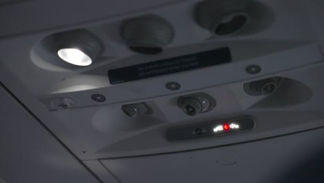 close up of seatbelt sign on and a reading light on in a commercial airplane at night