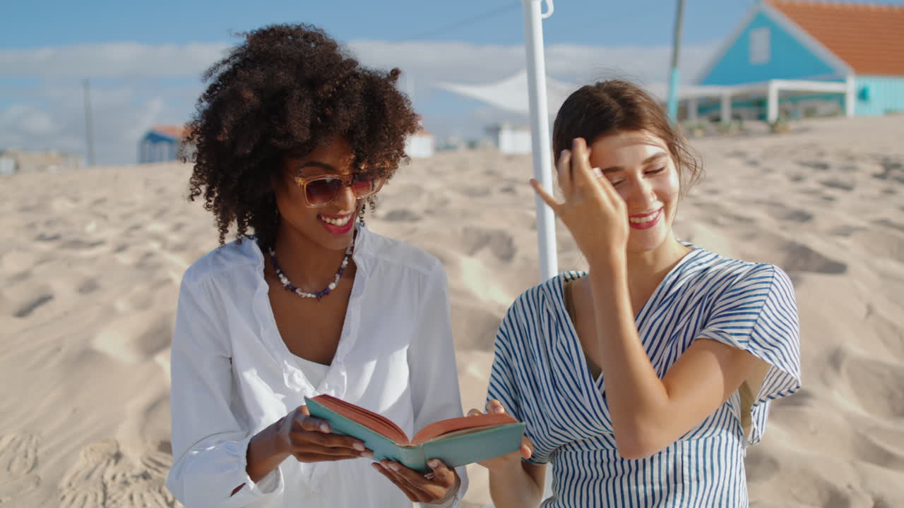 amigos disfrutando de un picnic libro en la playa de arena. chicas alegres divirtiéndose leyendo