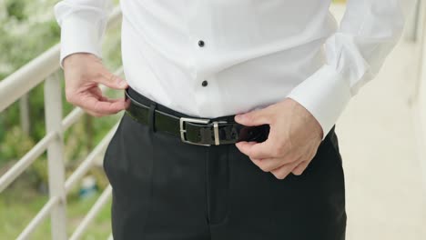 close up of a groom adjusting sleek black belt on tailored trousers during wedding prep