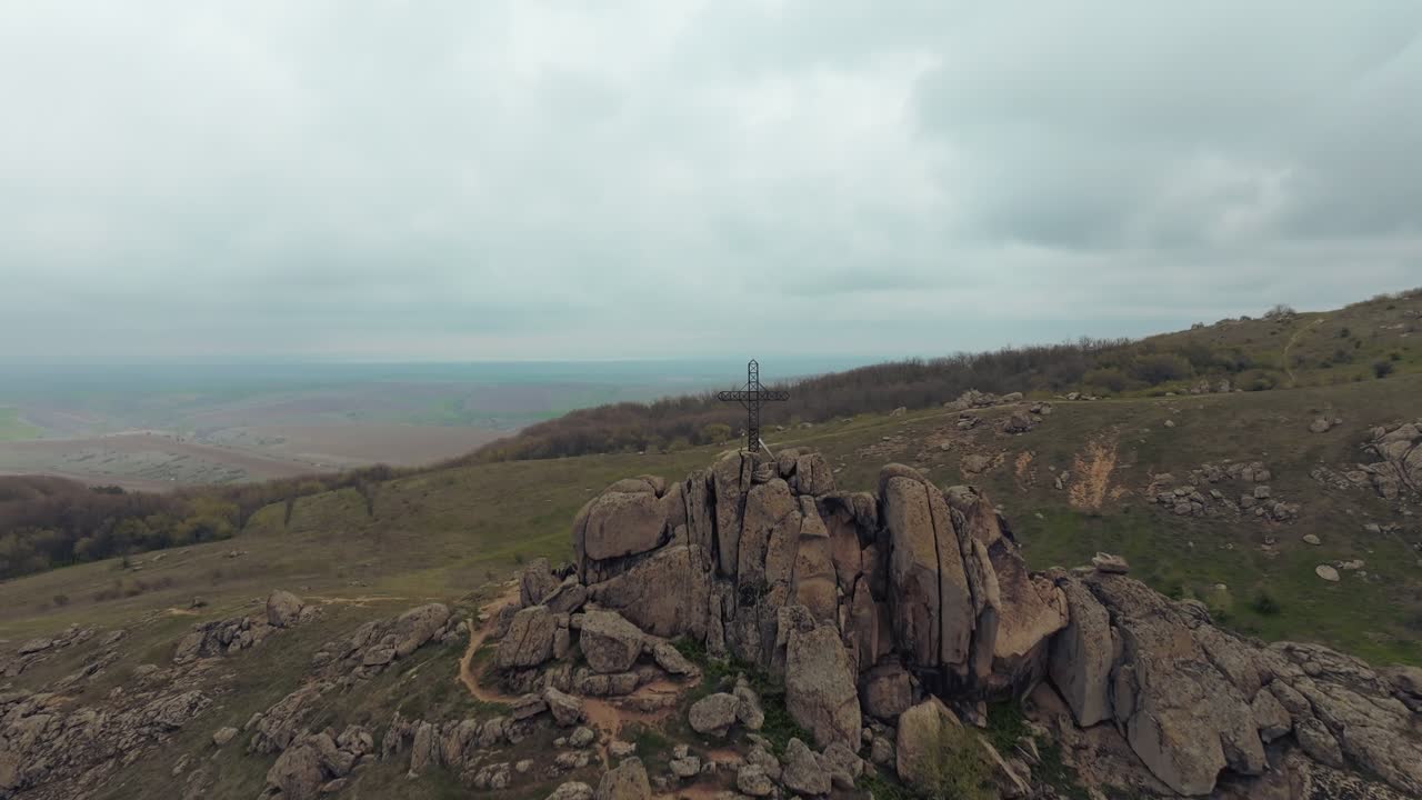 Ripresa rivelatrice con drone di una cima rocciosa coronata da una croce solitaria, che emerge contro un cielo coperto