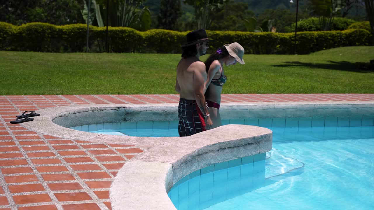 un hombre y una mujer entran en una hermosa piscina en un día caluroso y soleado de verano.