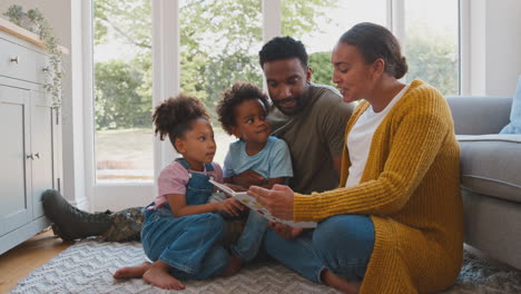 Army-Family-With-Pregnant-Mother-Sitting-On-Floor-In-Lounge-At-Home-Reading-Book-Together