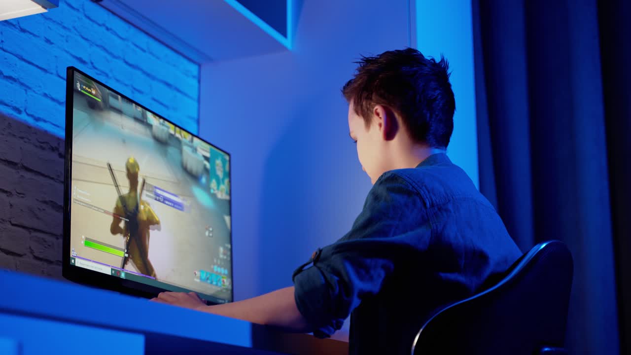Teen boy plays online game on computer at night. Side view of a gamer playing a video game in the room. Teenager becomes angry after losing in computer game.