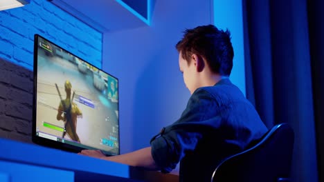 teen boy plays online game on computer at night. side view of a gamer playing a video game in the room. teenager becomes angry after losing in computer game.