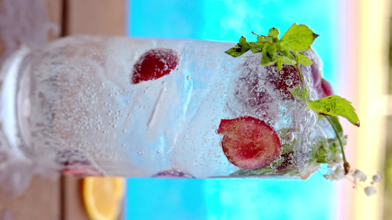 Mojito cocktail glass with ice and cherry and mint, soda and gin near a blue pool close up