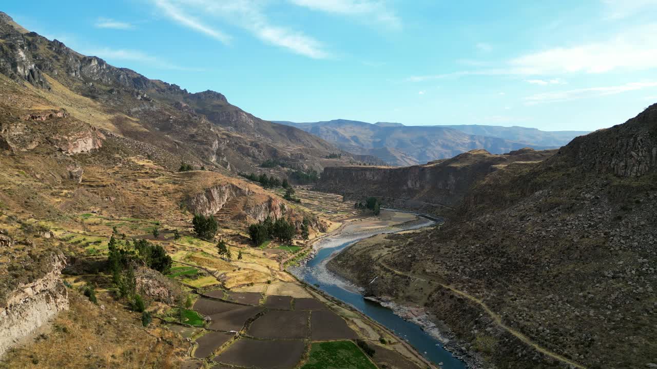 Aerial 4K shot of the Andes in Peru at sunrise, soft golden rays lighting up the valley floor and shimmering along a curving river