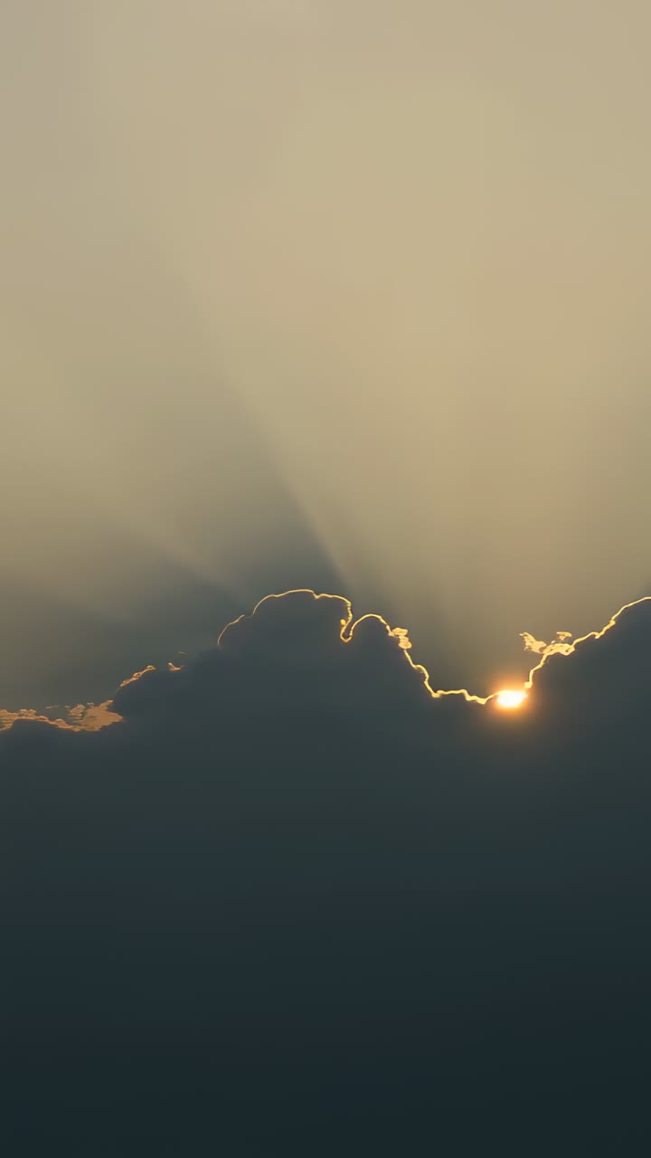 Vídeo vertical: luz solar rompendo um banco de nuvens, com o sol surgindo e emitindo raios ao nascer do sol