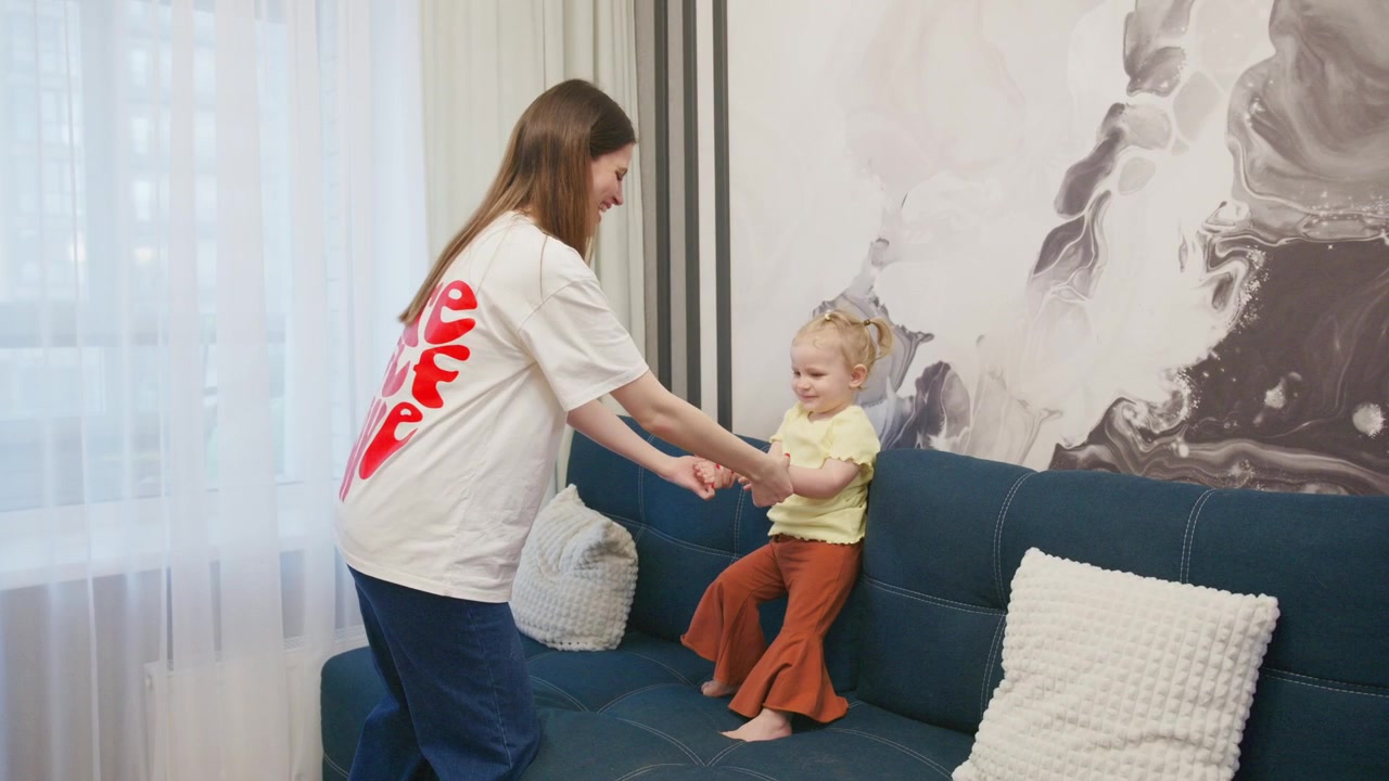 Mor og datter leker og hopper på sofaen hjemme
