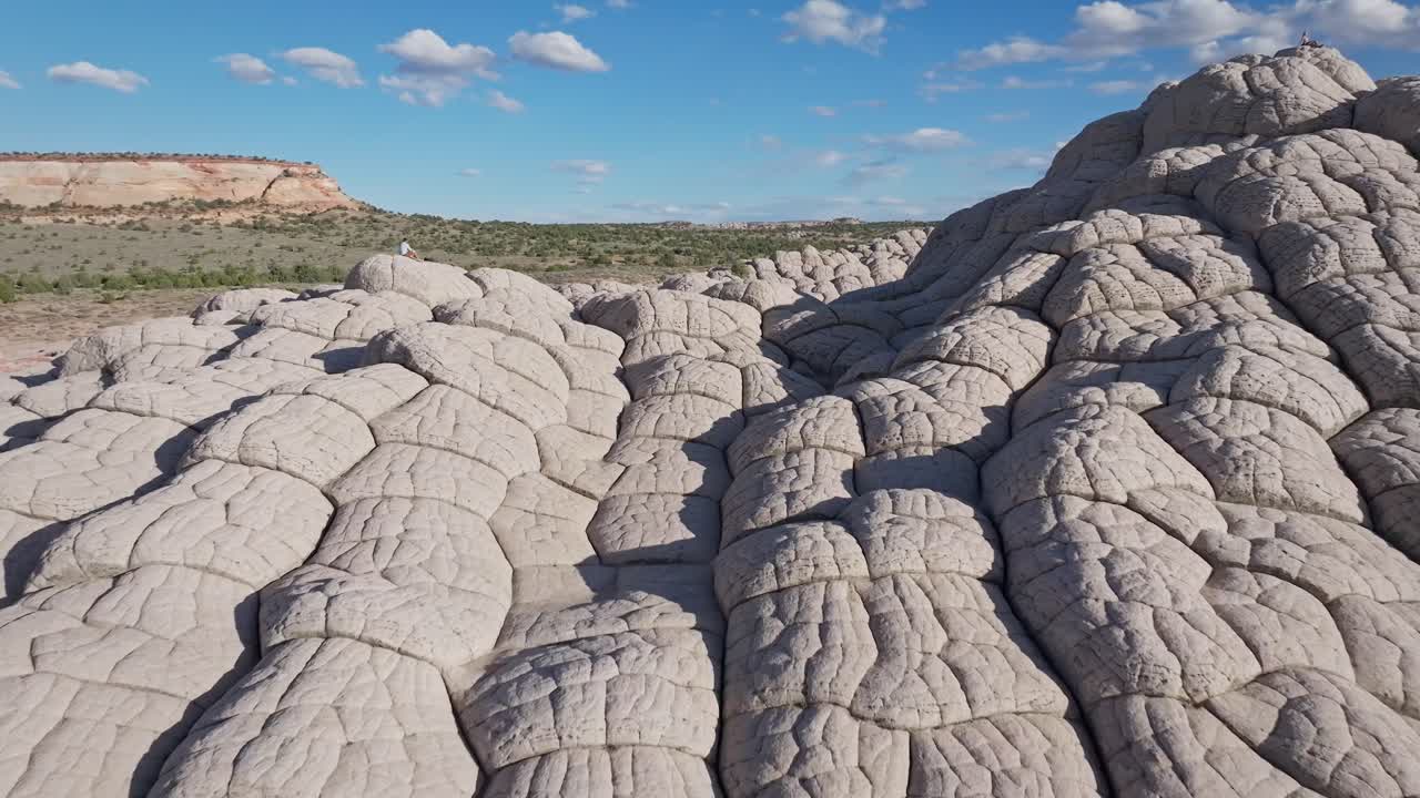 A close-proximity drone flyover of the unique sandstone rock features of White Pocket Arizona surrounded by sandy desert and blue skies