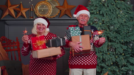 Smiling-married-senior-grandparents-man-woman-holding-Christmas-gift-boxes-and-bengali-sparkles