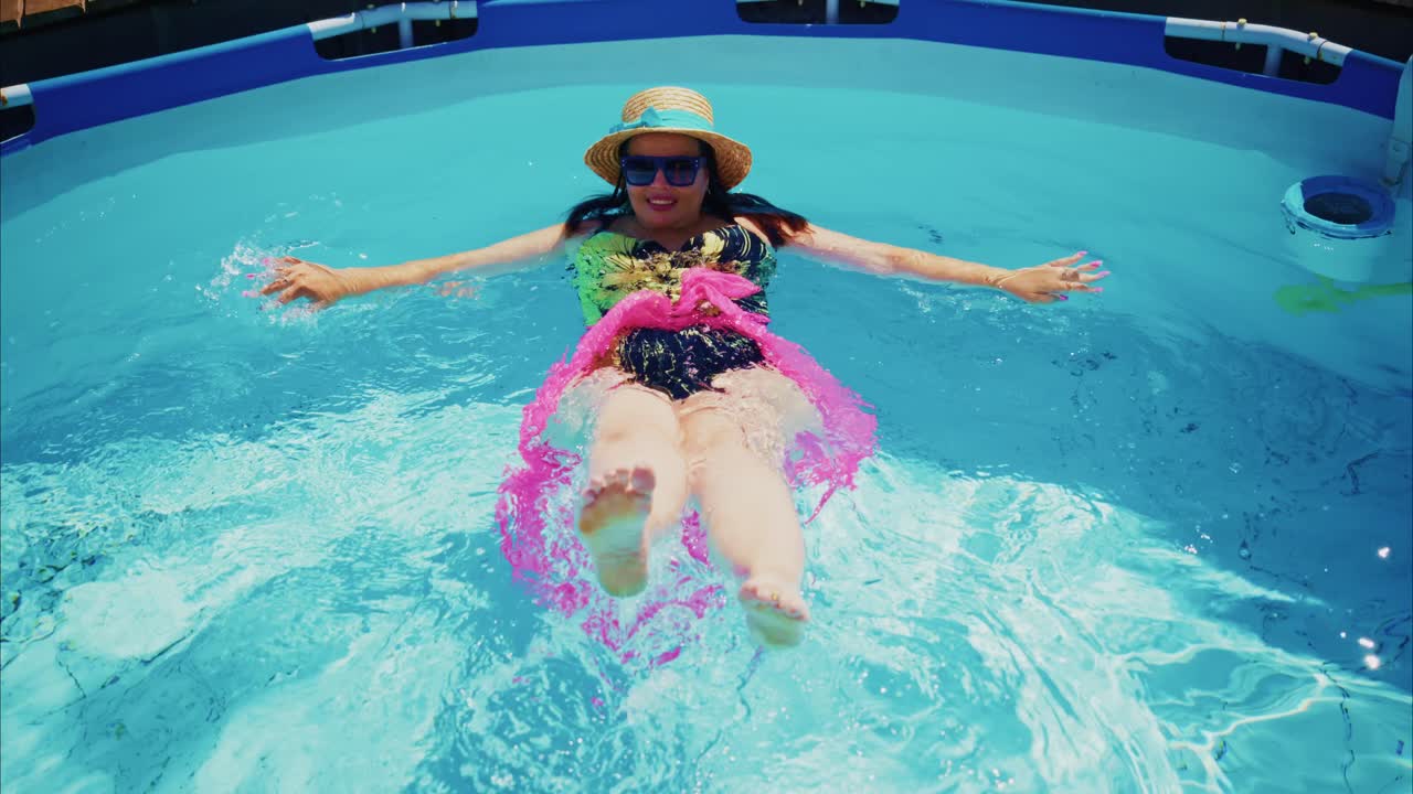 Woman relaxing in swimming pool wearing swimsuit and straw hat with vibrant water splashes