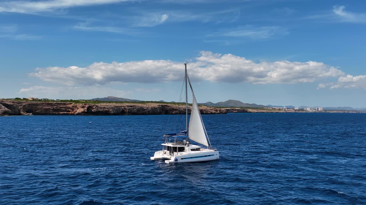 Filmato aereo di un catamarano che naviga al rallentatore su acque cristalline durante una giornata estiva e soleggiata a Maiorca