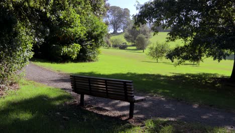 Un-Banco-Vacío-En-Un-Parque-Verde-Urbano-De-La-Ciudad-Haciendo-Turismo-Por-El-Sol-Sobre-La-Hierba-Verde