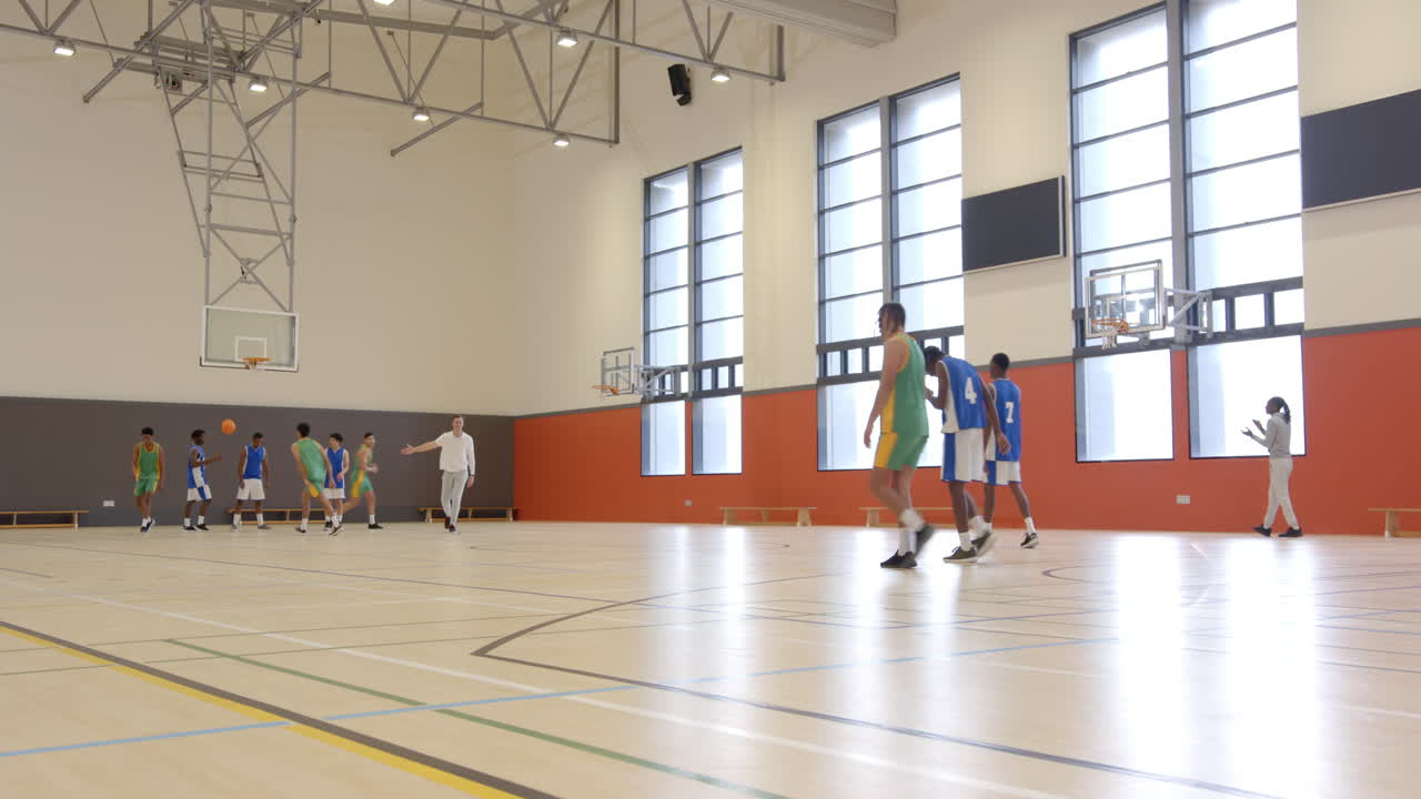 Playing basketball in school gym, students practicing with coach and teammates