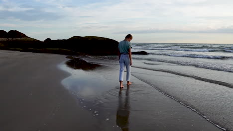 young girl walking toward ocean waves on sandy coastline, back view