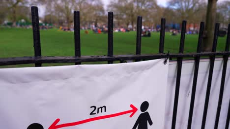 social distancing sign and people gathering in a park in london during the covid-19 coronavirus pandemic, not respecting lockdown, on a sunny spring day