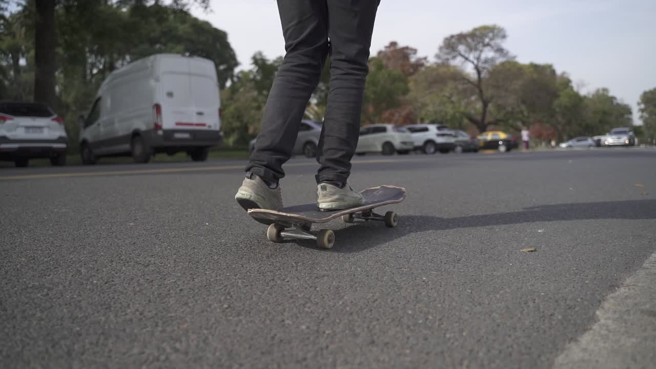 Primo piano delle gambe di uno skater in skateboard per strada con auto al tramonto