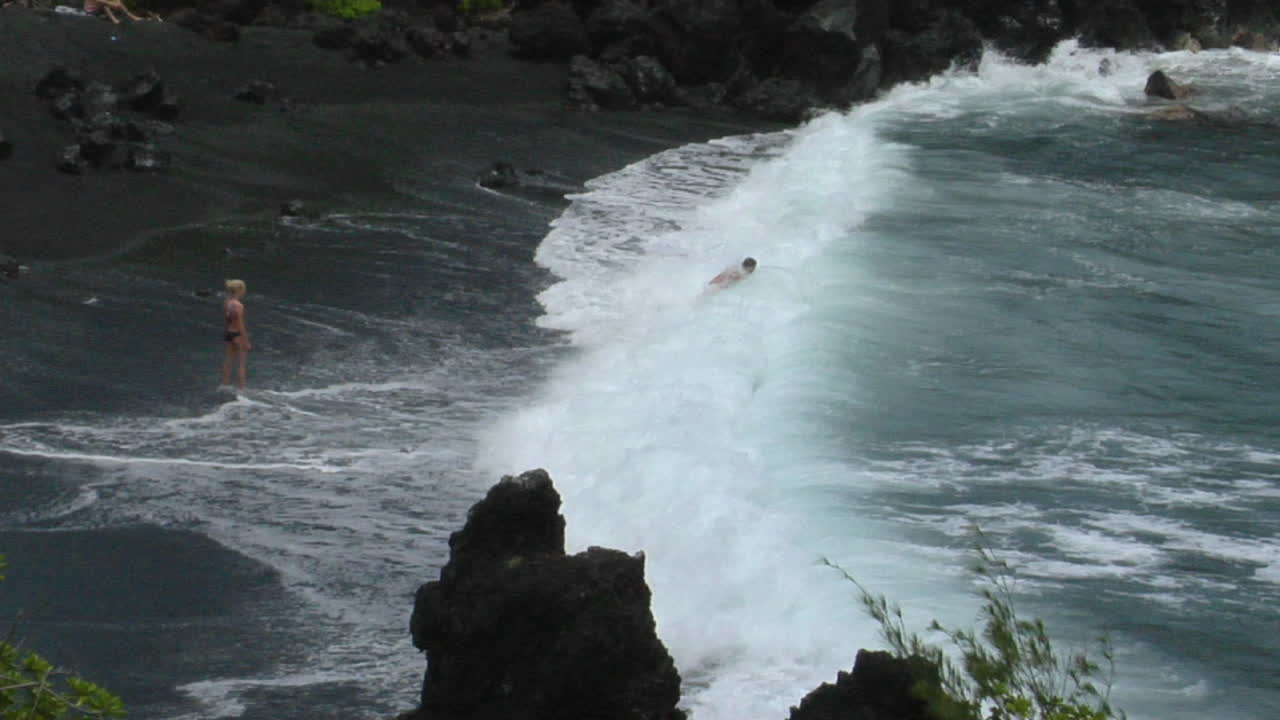 한 남자가 하와이의 검은 모래 해변을 따라 큰 파도와 싸웁니다.
