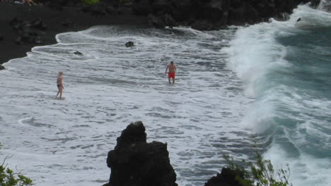 Un-Hombre-Lucha-Contra-Grandes-Olas-A-Lo-Largo-De-Una-Playa-De-Arena-Negra-En-Hawaii