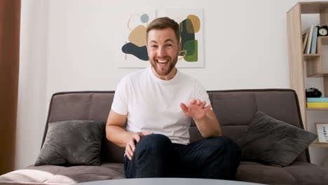 Handsome-Happy-Man-Sitting-On-Sofa-In-Living-Room-Looking-At-Camera-While-Having-A-Video-Call