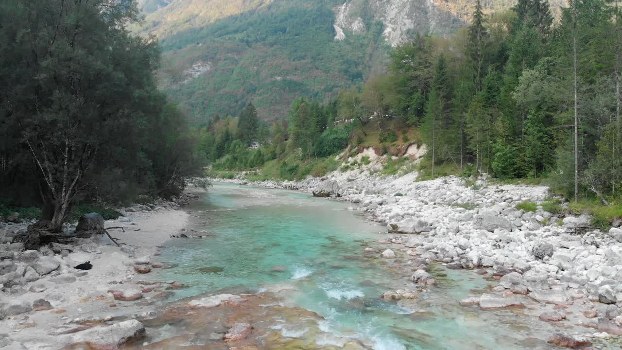 Drone che vola sopra il fiume Isonzo vicino a Trenta, con terreno accidentato e alberi ai lati.