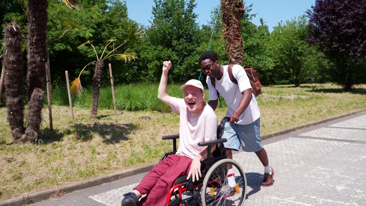 Young Man Pushing Friend in Wheelchair Through Sunny Park