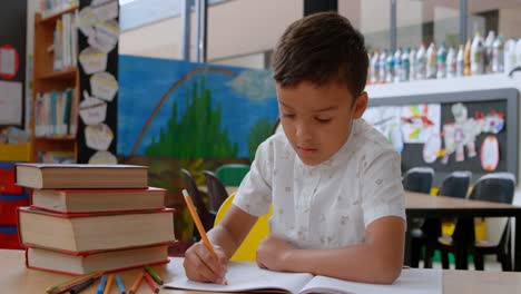 vista frontal de un escolar asiático levantando la mano mientras estudia en el escritorio en el aula de la escuela 4k