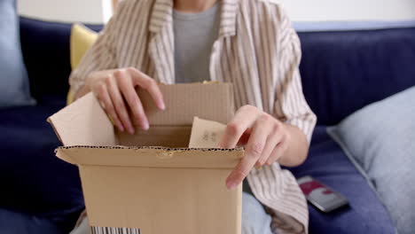 midsection of excited biracial man opening delivery in cardboard box, slow motion