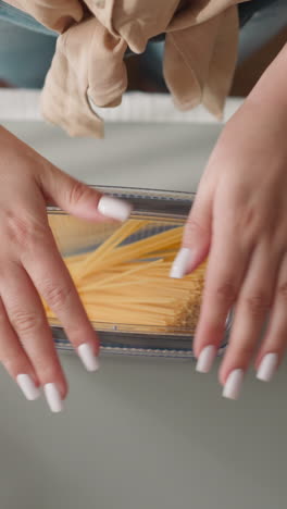 woman closes plastic container with raw spaghetti slow motion. female presses lid with hands fixing carefully and shakes watching movement of product upper view