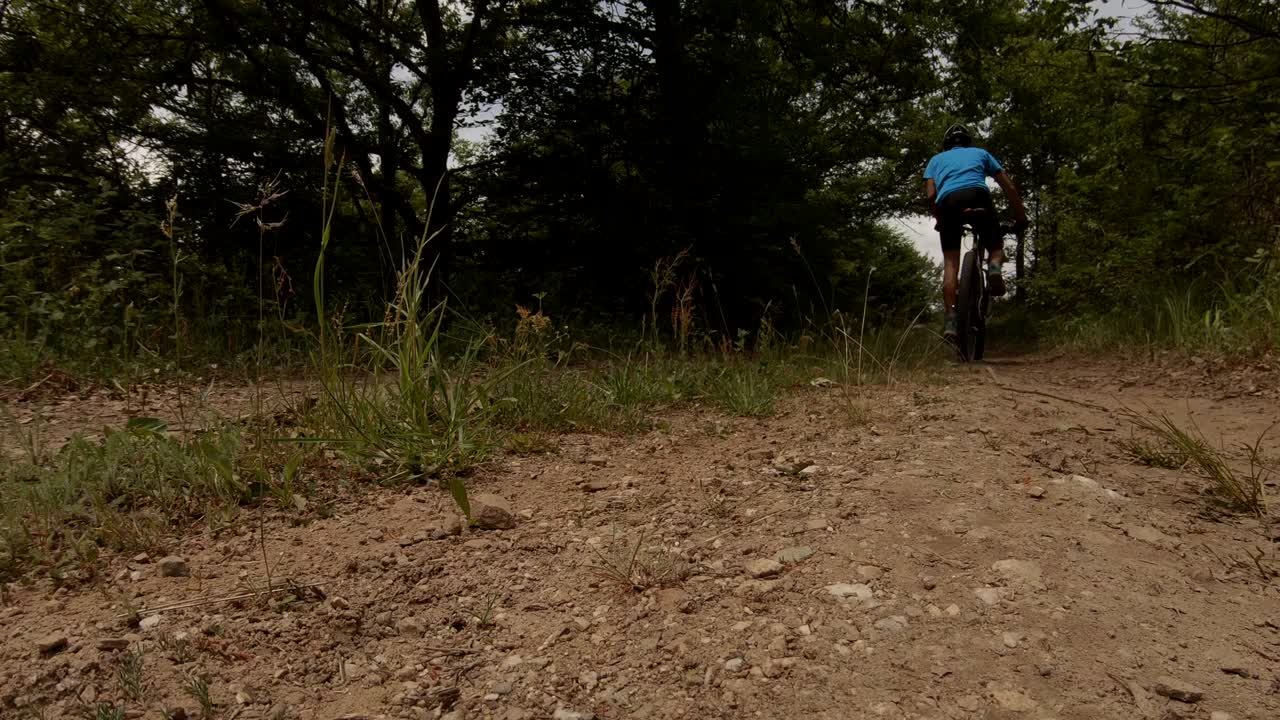 toma desde abajo de un ciclista en bicicleta lentamente por un camino de tierra en un día soleado de verano