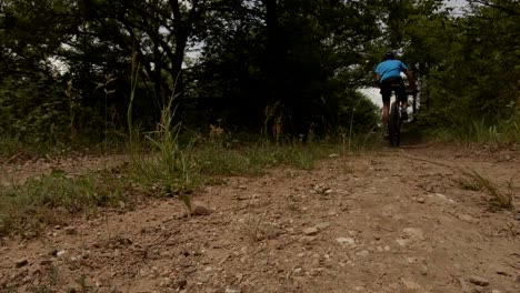 shot from below of a cyclist slowly cycling on a dirt road on a sunny summer day