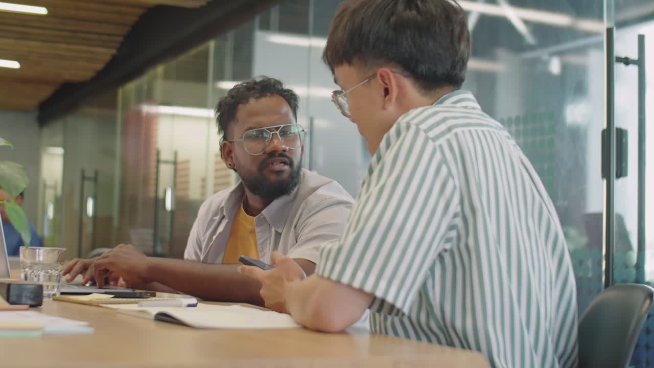 Two Men Using Laptop and Phone and Speaking in Coworking Room