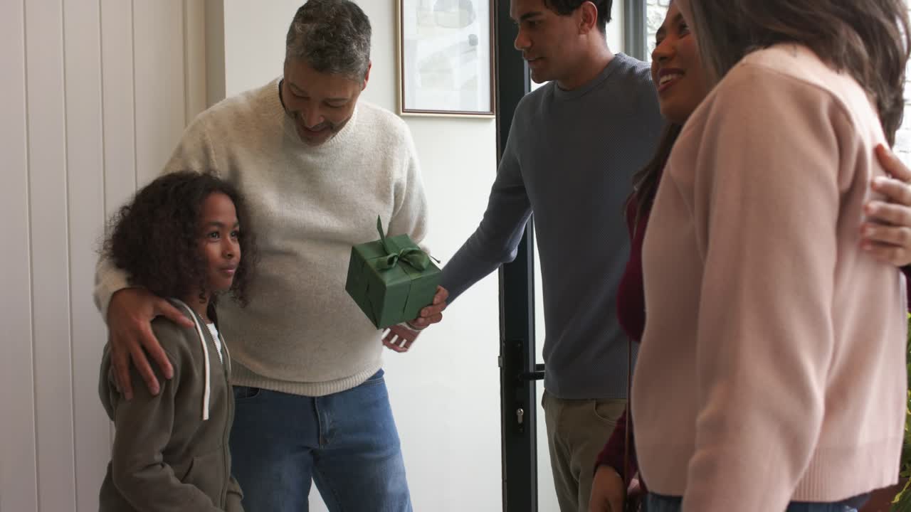 Entering foyer child greeting diverse family while senior man offering wrapped green gift box