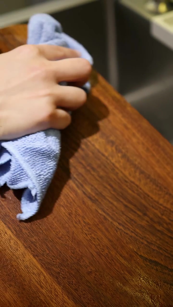 Close-up shot of hands using a blue microfiber cloth to dry a wet wooden board