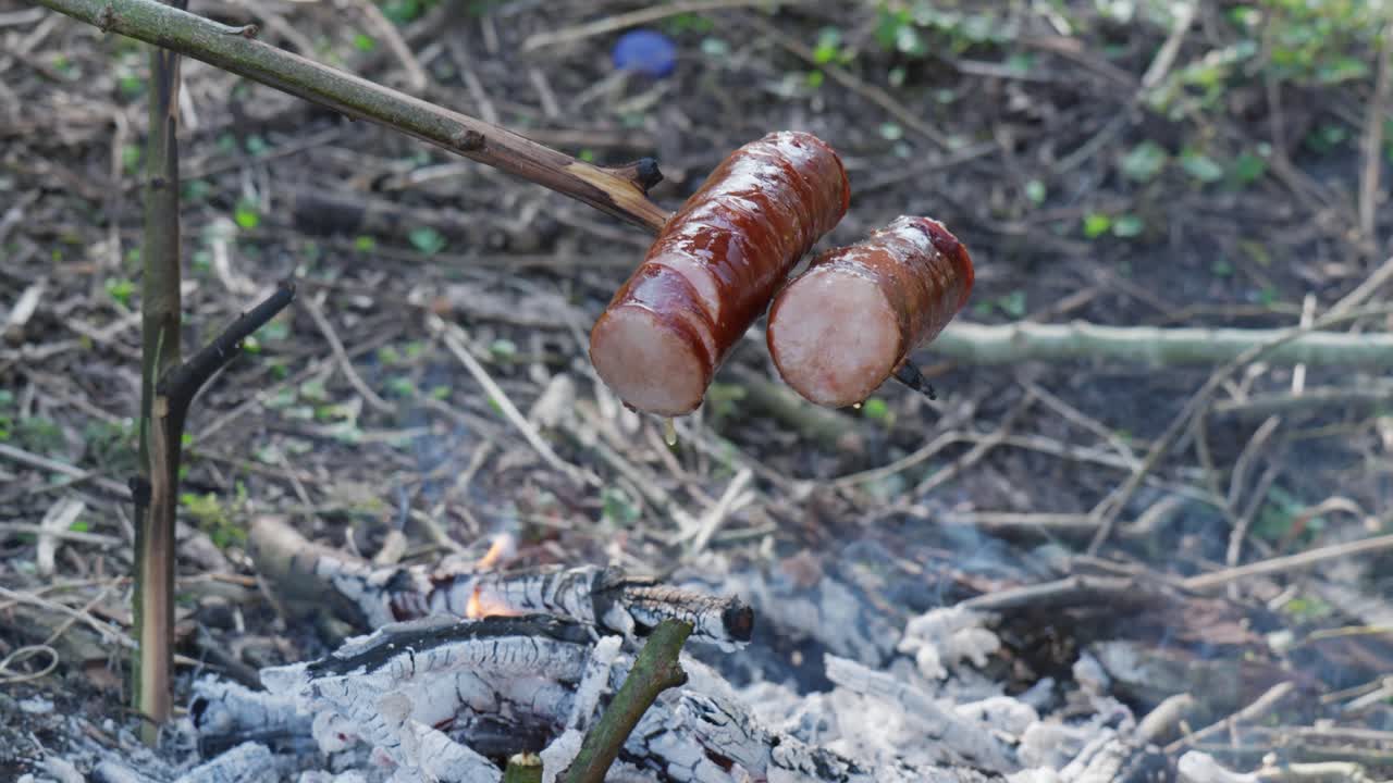 Grilling sausages over an open fire in the woods with smoke rising in the background