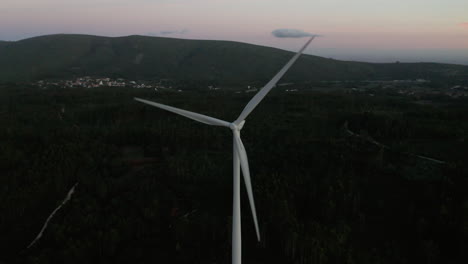 Turbinas-De-Viento-Girando-Lentamente-En-Un-Denso-Bosque-De-Follaje-Con-Un-Pueblo-Tranquilo-Al-Fondo-En-Serra-De-Aire-E-Candeeiros,-Leiria-Portugal