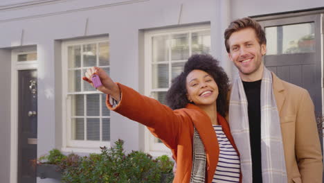 portrait of multi cultural couple outside house on moving day holding keys to new home in fall or winter - shot in slow motion