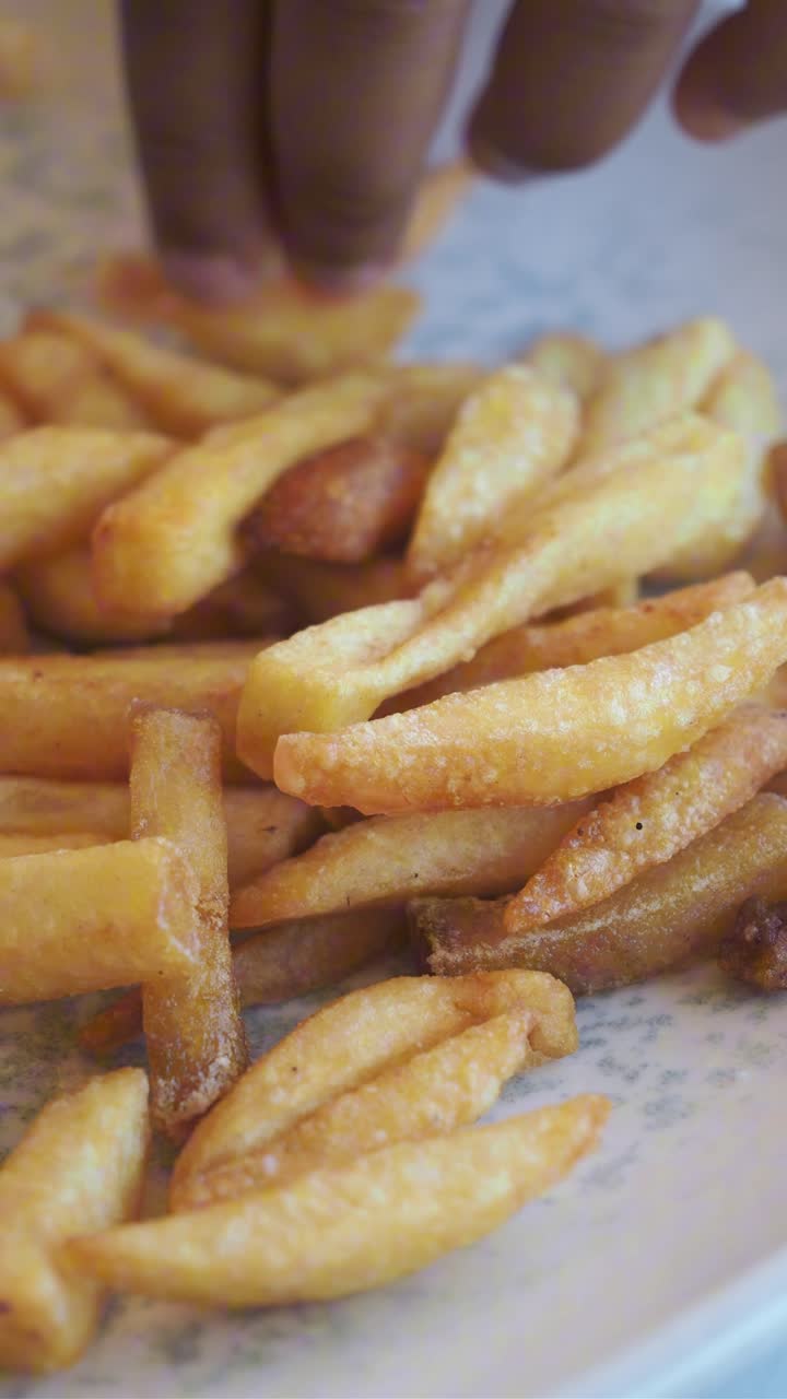 Mano recogiendo una patata frita dorada de un plato