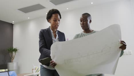 two african american female architects discussing blueprints in office, in slow motion