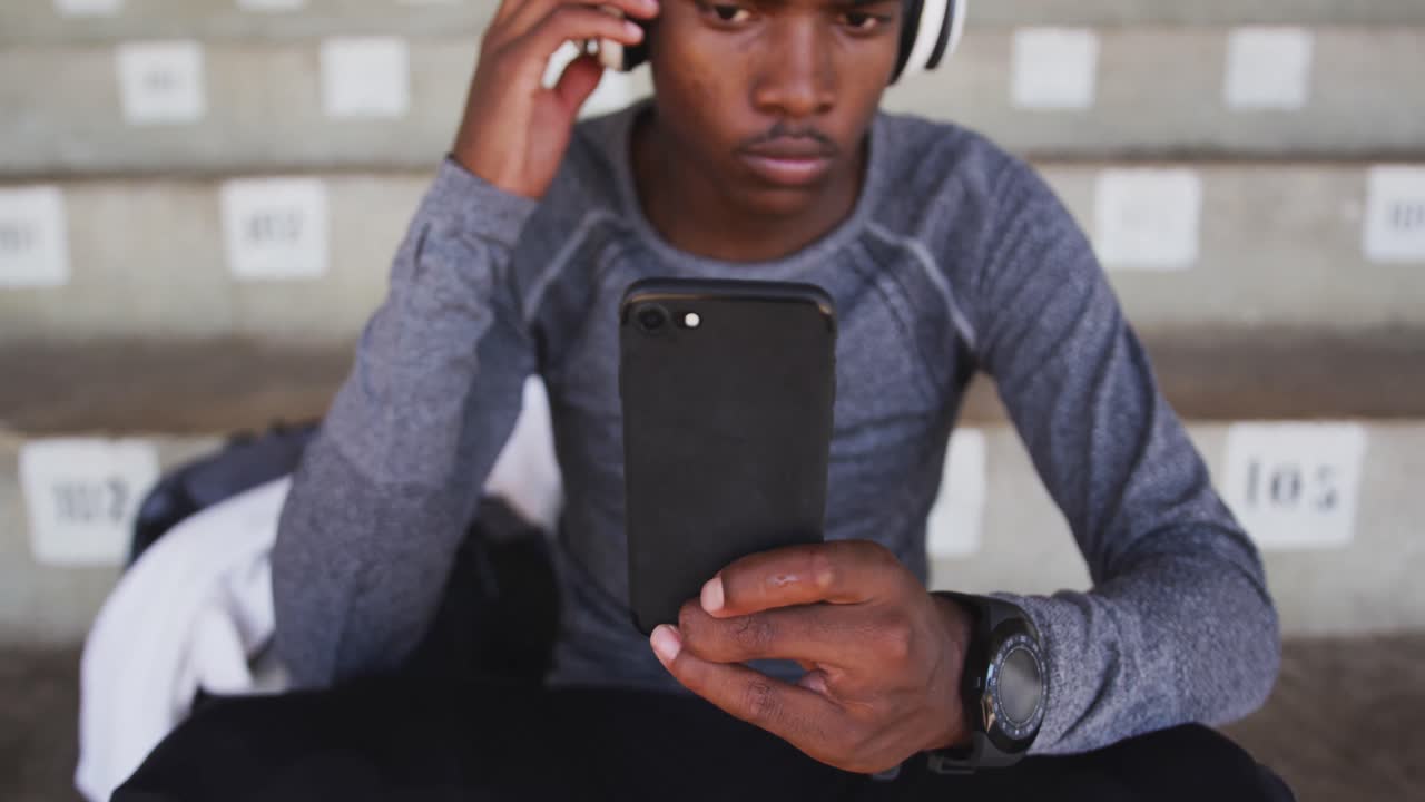 Disabled mixed race man with prosthetic legs sitting on a stadium and using a smartphone