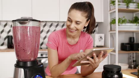 woman using a tablet and preparing smoothie at kitchen