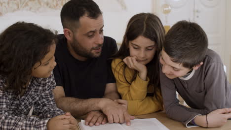 patient father studying with cheerful children at home.