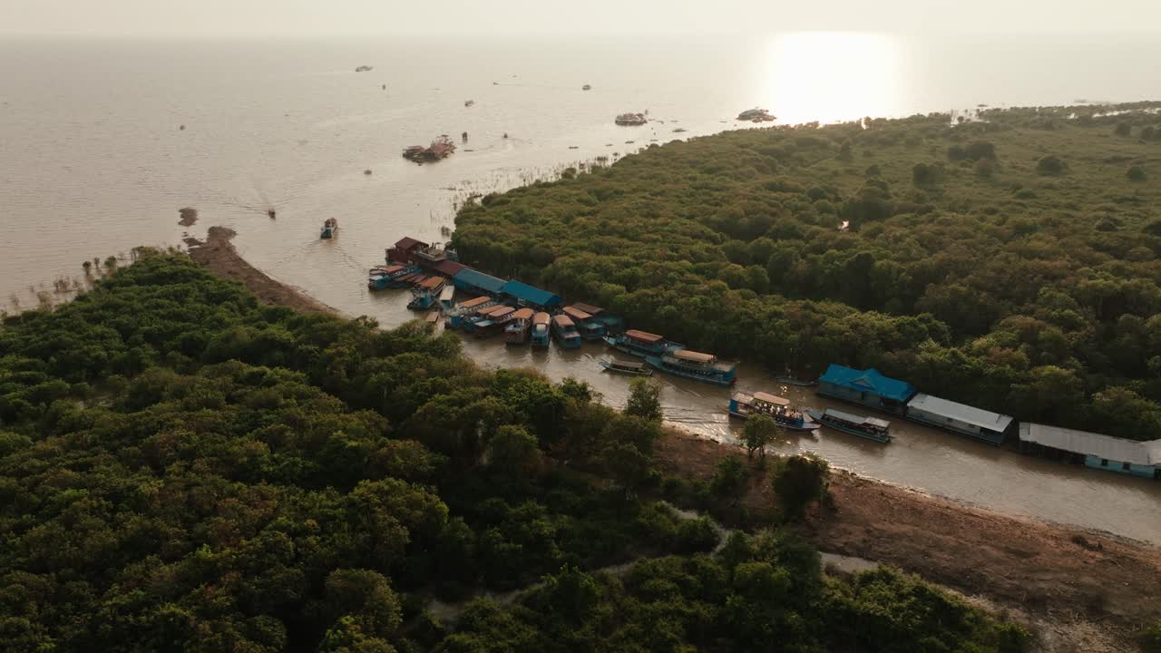 Tour boats navigate mangrove waterways toward Tonle Sap lake at golden sunset in Cambodia