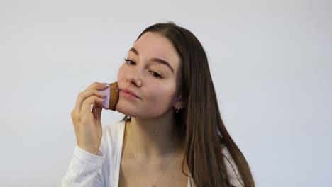 Attractive-young-woman-doing-her-morning-makeup-with-the-brush-in-front-of-the-mirror,-white-background