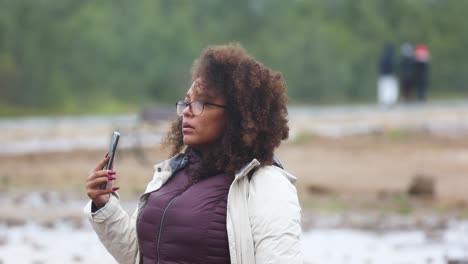 Una-Mujer-De-Raza-Mixta-Lleva-Una-Chaqueta-De-Viaje-De-Invierno-Mientras-Filma-Con-Su-Teléfono-Inteligente.