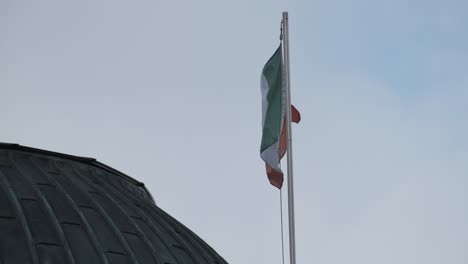 Irish-flag-on-a-rooftop-moving-with-wind,-daylight