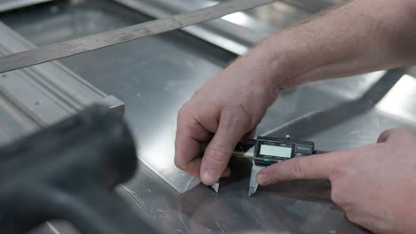 Worker's-hands-making-round-marks-on-an-aluminum-metal-sheet-with-caliper---closeup,-marking-lines-for-hole-saw-center-cutting