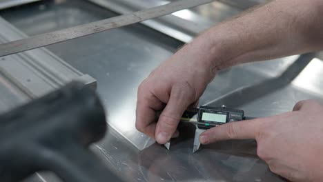 worker's hands making round marks on an aluminum metal sheet with caliper - closeup, marking lines for hole saw center cutting